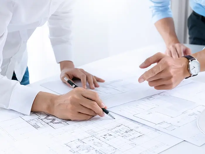 An image of two designers discussing factory construction plans with a blueprint.