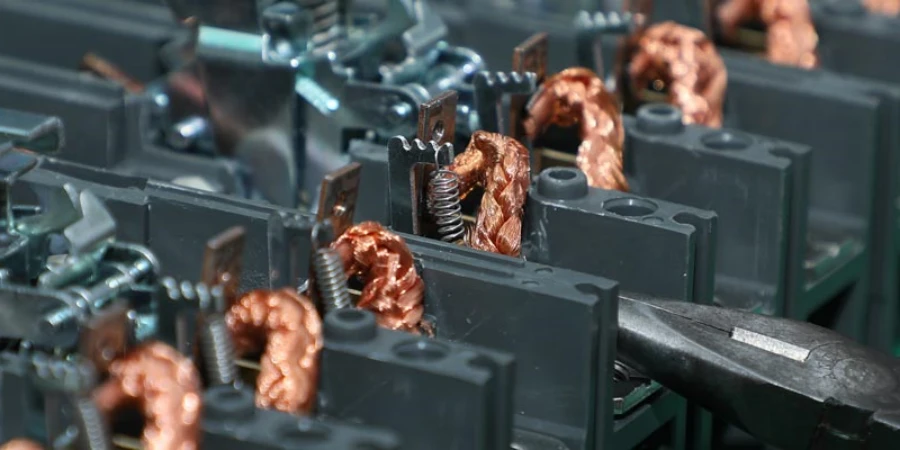 Close-up of MCCB circuit breakers being assembled on a production line, showing copper coils, metal screws, and plastic casings with a tool nearby.