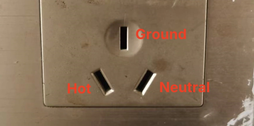 A wall-mounted electrical outlet with three labeled slots: Ground at the top, Hot on the bottom left, and Neutral on the bottom right.