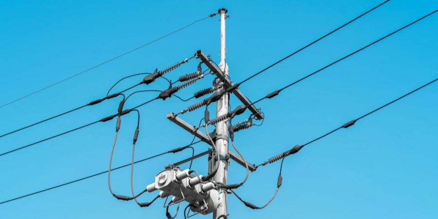 A tall electrical power line pole with multiple wires and insulators, set against a bright blue sky