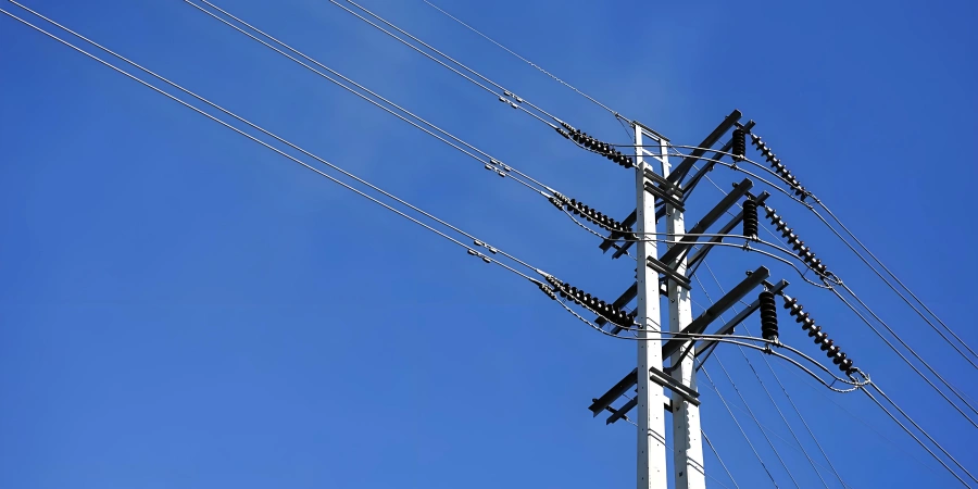 A tall concrete power line tower with multiple crossarms and insulators, supporting several high-voltage electrical wires, set against a clear blue sky.