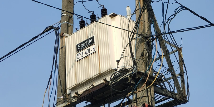 A utility pole with a Starlite 2013-400-H transformer mounted on it, surrounded by numerous electrical wires and cables, against a clear blue sky.