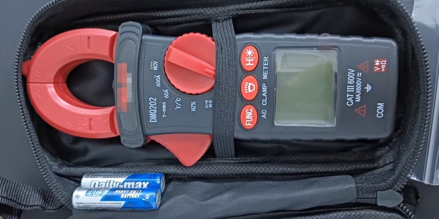 A black and red clamp meter with a digital display and buttons, stored in a case with two batteries.