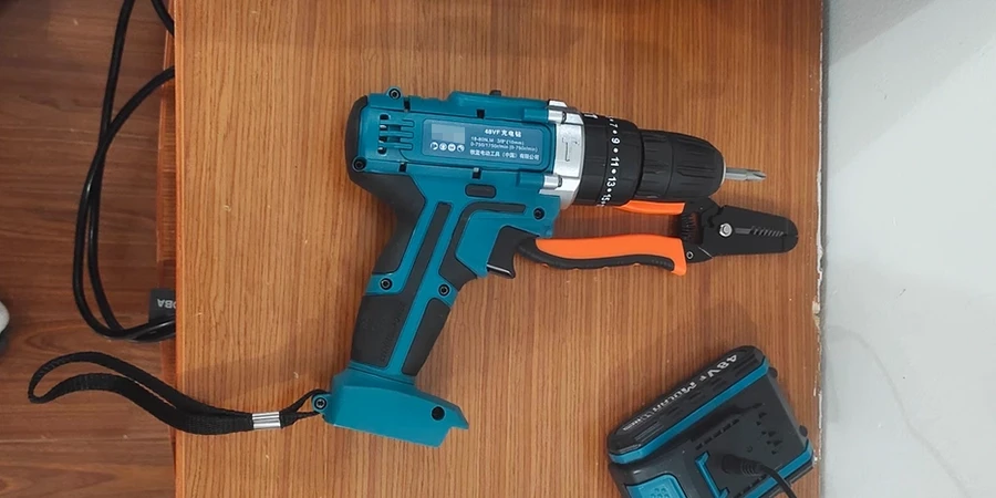 A blue cordless drill with an orange handle, placed on a wooden surface, accompanied by a black wire stripper and a matching blue battery pack.