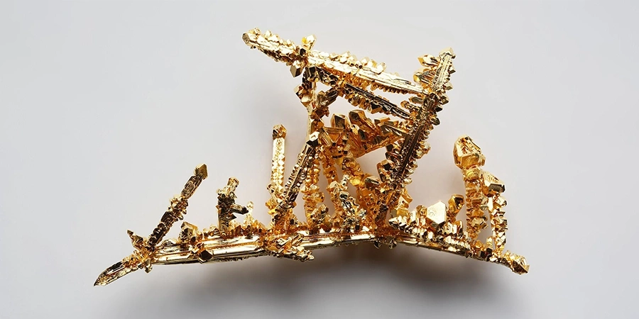 A intricate, naturally formed gold crystal structure with sharp, jagged edges, displayed against a plain white background.