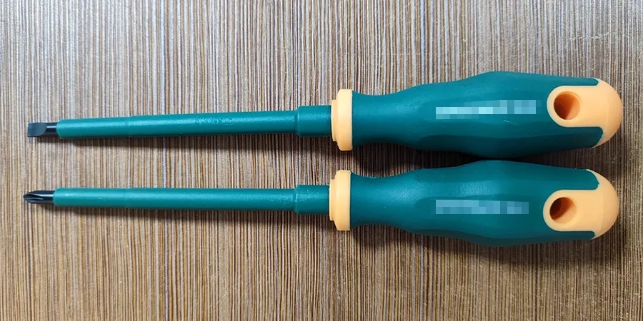Two green-handled screwdrivers with orange accents, one with a flathead and one with a Phillips head, placed on a wooden surface.