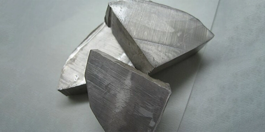 Several irregularly shaped, shiny sodium metal pieces with a metallic surface, placed on a plain background.