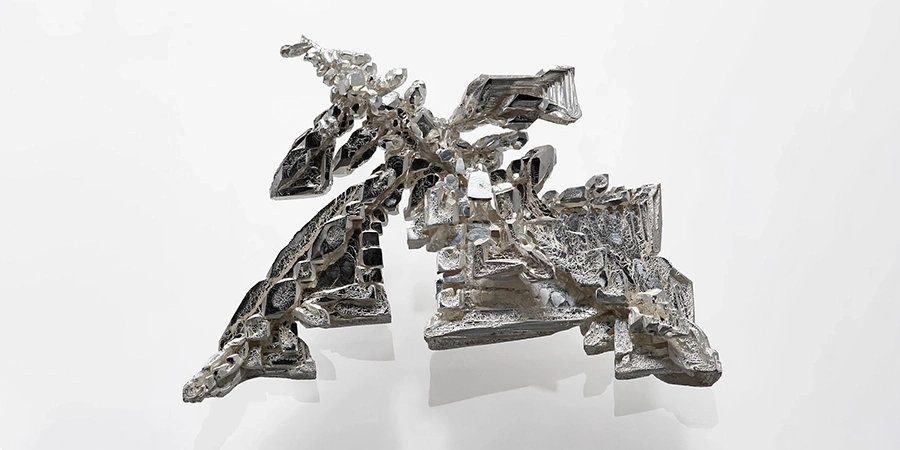 A complex, jagged silver crystal structure with a metallic sheen, displayed against a plain white background, showcasing its natural geometric patterns.