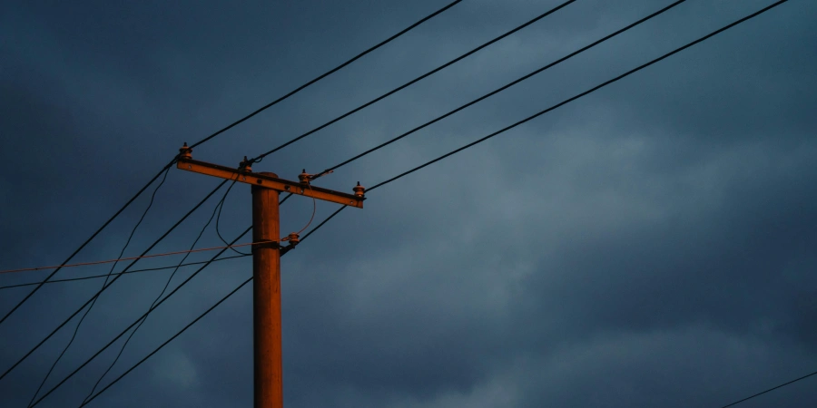 A wooden utility pole with multiple power lines extending from it, set against a dark, cloudy sky suggesting an impending storm. The scene implies weather conditions that could impact breaker tripping.