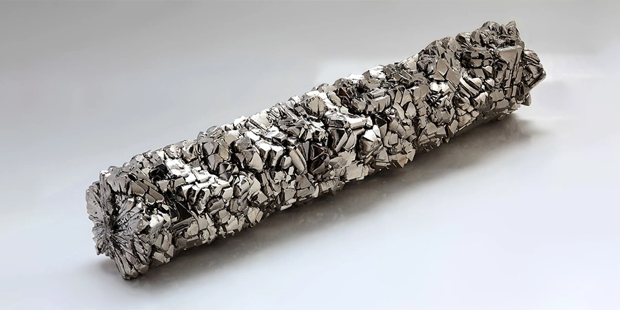 A long, cylindrical titanium crystal rod with a rough, metallic, and jagged surface, displayed on a plain white background.
