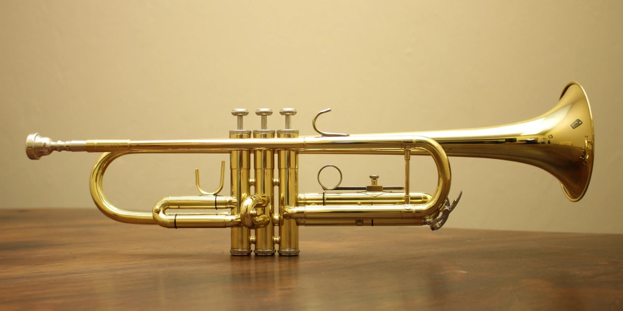 A polished brass trumpet resting on a wooden table, featuring three valves, a curved bell, and a sleek design, ready for a musical performance or display.