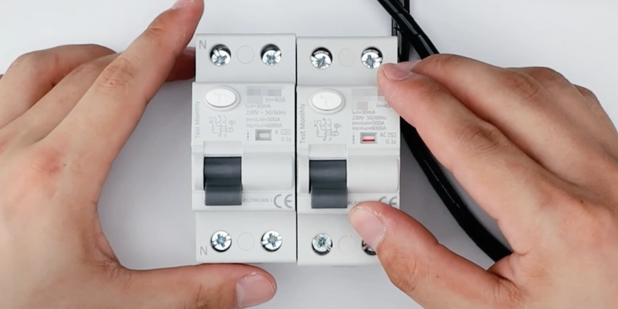 Two residual current circuit breakers rated at 40A and 30mA, held by hands, with black switches in the OFF position, orange test buttons, and technical specs including 230V voltage, placed against a white background with a black wire visible.