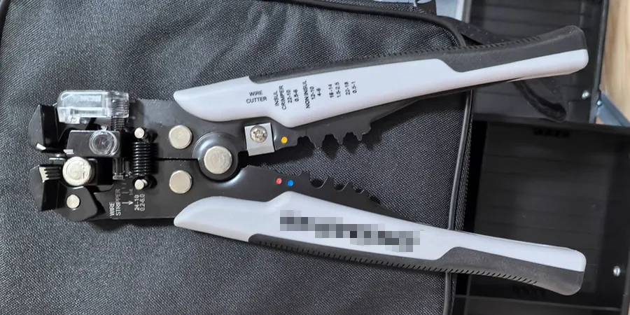 A wire stripper and cutter tool with black and white handles, featuring multiple adjustment knobs and a cutting blade.