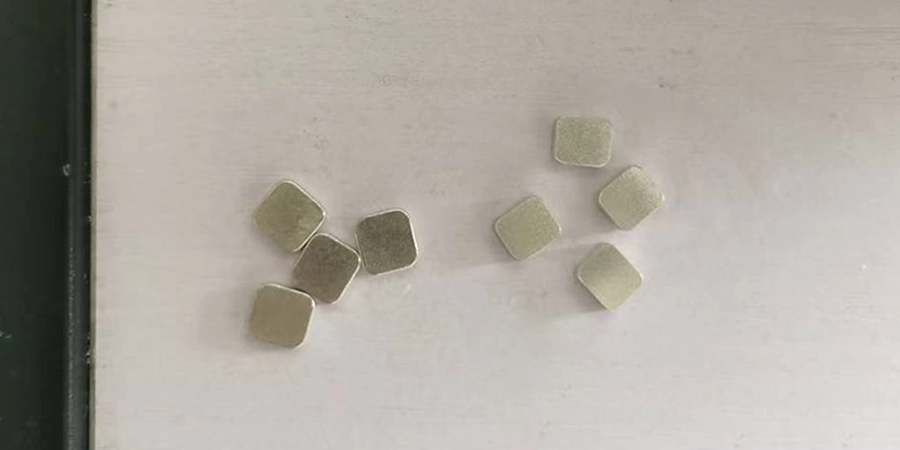 Eight small, square, metallic moving and fixed contacts for a Molded Case Circuit Breaker (MCCB) scattered on a white surface, with a dark edge visible on the left side.