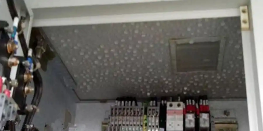 Inside view of an electrical cabinet showing water droplets on the metal ceiling. Below are mounted circuit breakers and terminal blocks with wires.