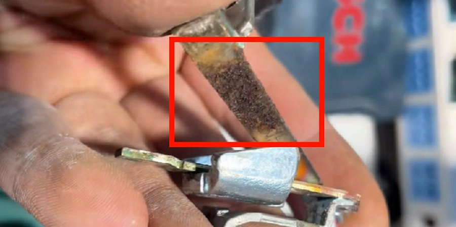 Hand holding a metal part from a circuit breaker. Red box highlights bimetal strips with black corrosion and rust from moisture damage.