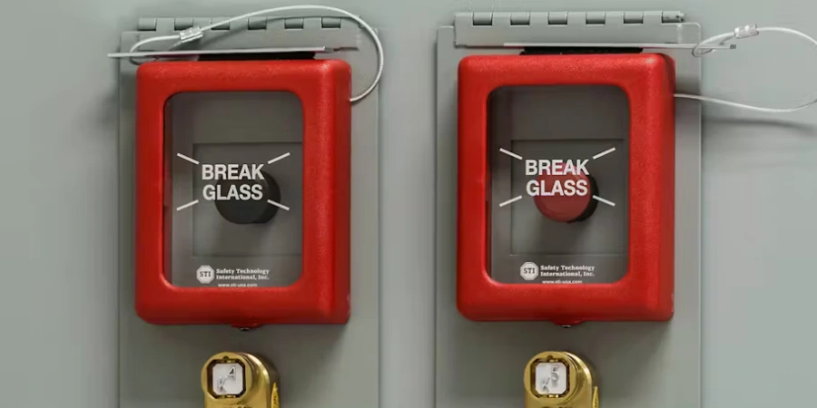 Two red protective covers from Safety Technology International (STI) mounted on a gray electrical panel, each featuring a 