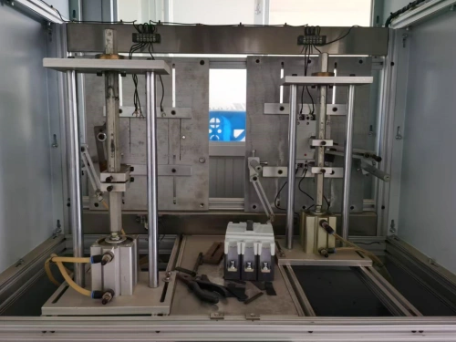 A mechanical endurance test device for molded case circuit breakers (MCCBs), featuring a metallic frame with adjustable arms and clamps holding an MCCB unit, set against a background with a blue window visible.