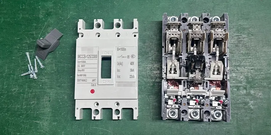 A green surface displaying parts of an MCCB-125/300 molded case circuit breaker, including a white front panel with 
