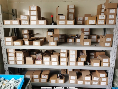 A warehouse shelf unit filled with cardboard boxes and containers holding various accessories for molded case circuit breakers (MCCBs), neatly labeled and organized across multiple levels, with some open boxes revealing small components and wires.