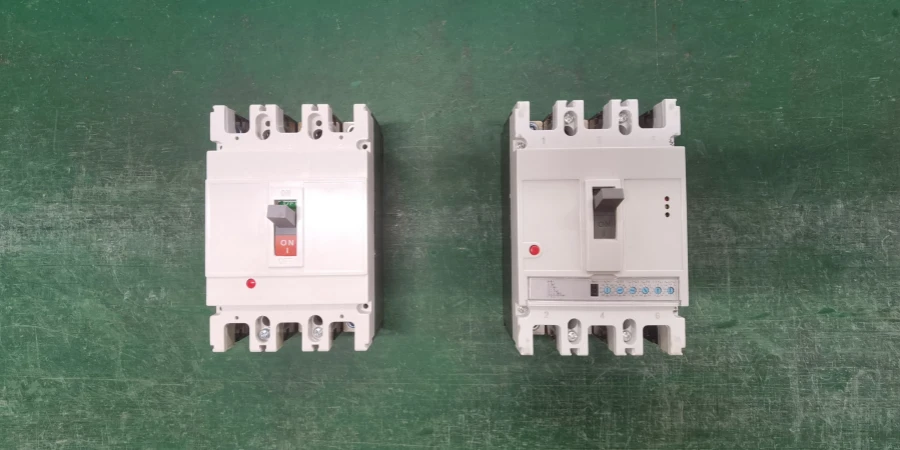 Two white molded case circuit breakers on a green surface. The left is a standard MCCB with a red 'ON' switch and red indicator light. The right is an electronic MCCB with a gray switch, red indicator light, and blue status lights.