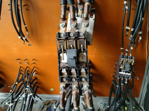 A close-up view of a temperature rise test bench for molded case circuit breakers (MCCBs), featuring a central MCCB unit with multiple copper connectors and black cables attached, mounted against an orange panel.