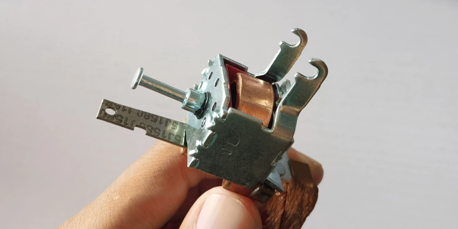Hand holding a small thermal-magnetic trip unit for MCCB. Shows copper coil for magnetic trip, metal plunger