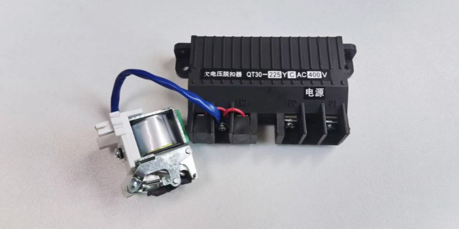 A black rectangular undervoltage trip module labeled "QT30-225YCAC400V" with Chinese text indicating voltage specifications, mounted on a white plastic housing containing a silver electromagnetic coil. Blue and red wires extend from the assembly, positioned on a light gray surface, designed to automatically trip a Molded Case Circuit Breaker (MCCB) during low voltage conditions for electrical safety.