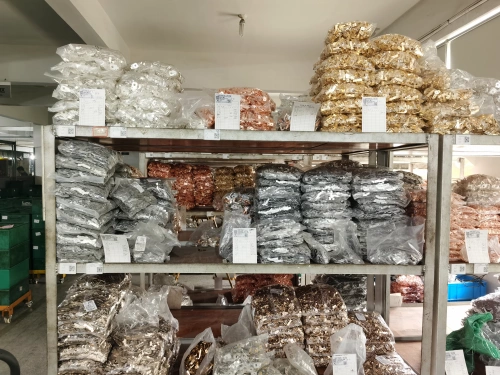 A warehouse shelf displaying stacks of iron and copper components for molded case circuit breakers (MCCBs), organized in plastic bags and labeled, with a variety of metallic parts in silver, copper, and bronze tones.