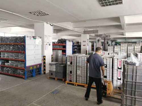 A warehouse with rows of orange and blue shelving units filled with semi-finished molded case circuit breakers (MCCBs), featuring a worker operating a forklift among stacks of grey components.
