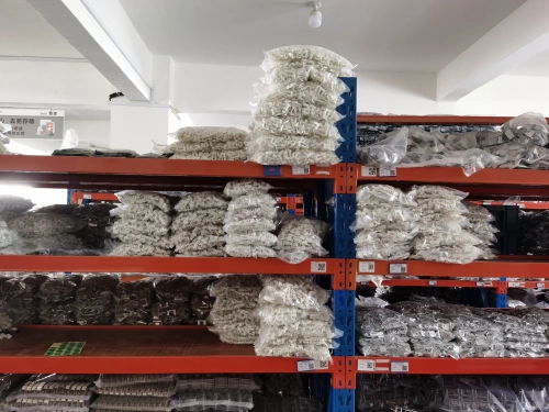 A warehouse shelf with orange supports, stocked with stacks of semi-finished molded case circuit breaker (MCCB) parts, primarily white and metallic components, organized in plastic bags and labeled for inventory.