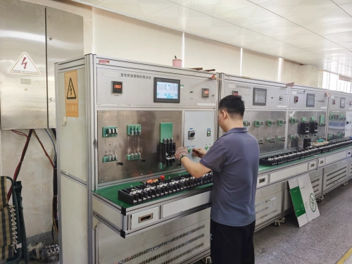 A photo of a technician in a gray shirt working at an Instantaneous Trip Test Bench, testing an MCCB (Molded Case Circuit Breaker). The bench features a control panel with a digital display, multiple switches, and electrical components. A warning sign with a lightning bolt is visible on the left side, and the setup is located in an industrial lab with tiled flooring and additional testing equipment in the background.