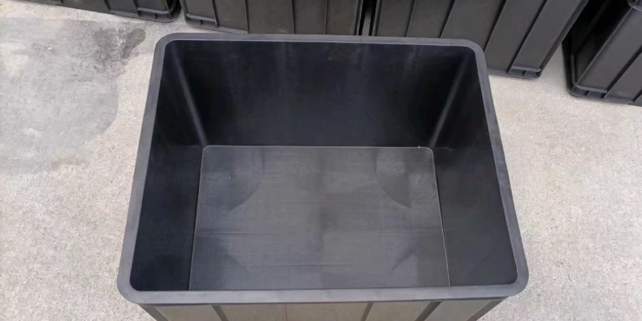Top-down view of an empty black anti-static plastic storage box on a concrete floor. Other similar boxes are stacked in the background.