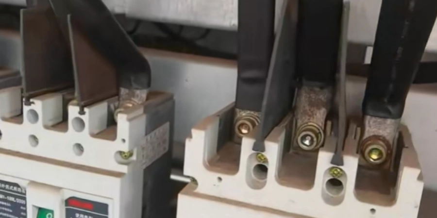 Close-up of a heavily corroded electrical terminal and busbar connection. Thick green and white corrosion covers the bolts and metal surfaces, with large areas of blackened burn marks, charred residue, melted insulation, and flaking paint, showing clear signs of long-term oxidation and overheating damage.