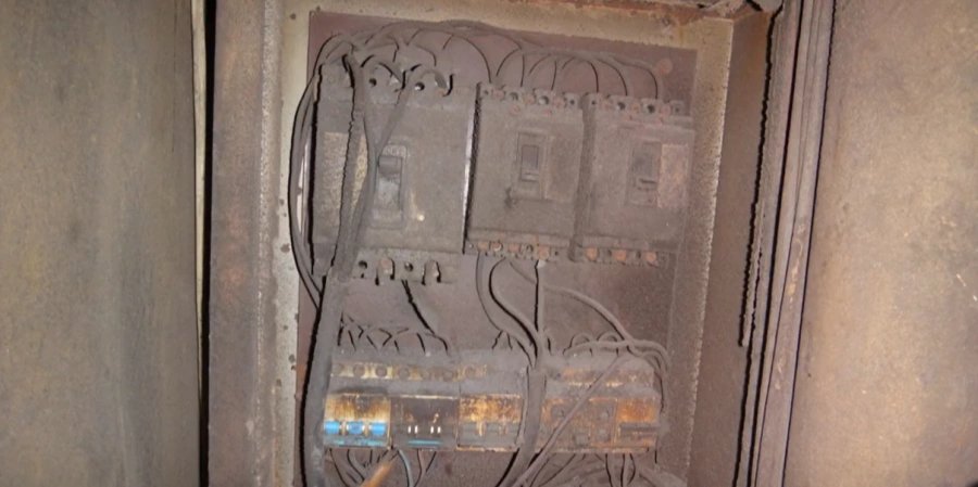 Inside view of an open electrical distribution panel completely covered in thick dust and dirt. Multiple circuit breakers, terminal blocks, and wires are visible, all coated in a heavy layer of gray dust.