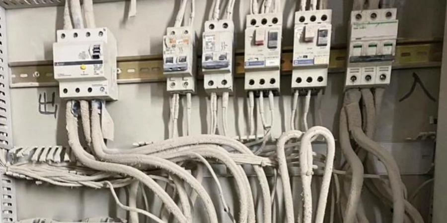 Close-up of a very dusty distribution board showing five breakers on a DIN rail: from left to right – one residual current device (RCD) with test button, followed by two standard MCBs, then two motor protection circuit breakers (MPCBs) in the third and fourth positions, and another breaker on the right; all devices and white wiring heavily coated in thick gray dust.