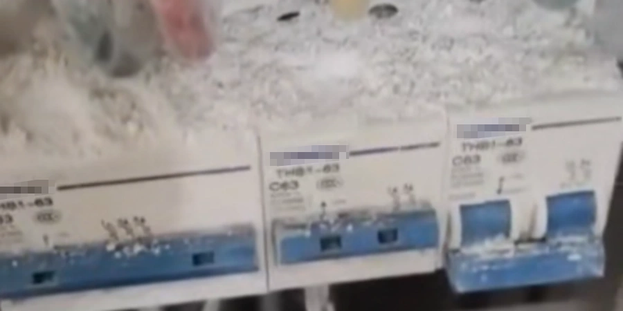 Close-up of a very dirty home electrical distribution board showing several blue C63 circuit breakers completely covered in a thick layer of gray dust and cobwebs, with some labels blurred for privacy.