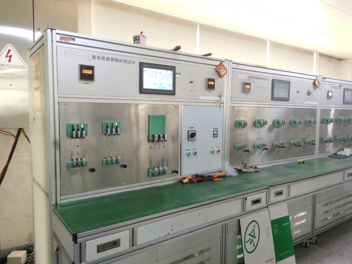 A metal test bench for MCCB instantaneous tripping, featuring a central digital screen, rows of green terminal blocks and switches, and screwdrivers on the green surface. Chinese labels and safety signs are present.