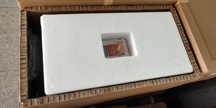 Open cardboard box with white foam insert. A white MCCB with red handle is visible through a cutout in the foam, ready for shipping.