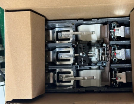 MCCBs in SKD (semi-knocked down) form without front covers, securely packed in a cardboard box with foam inserts. The internal mechanisms, silver operating handles, arc chutes, and red trip indicators are fully assembled and visible, ready for customers to attach the covers.