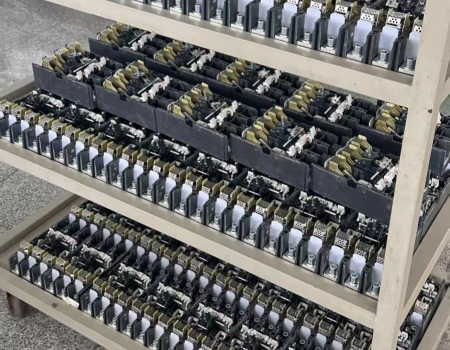 A rolling metal rack with multiple shelves holding trays of nearly finished MCCB SKD (semi-knocked down) units. Each unit is fully assembled with internal mechanisms, contacts, trip units, and terminals exposed, ready for customers to attach the front covers and complete the breakers.