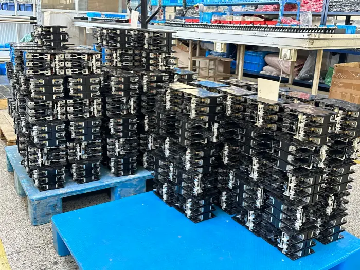 Piles of black skd molded case circuit breakers stacked on blue pallets in a warehouse, showing exposed metal terminals and assembly parts, with storage shelves in the background.