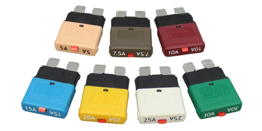 Seven color-coded automotive blade-style manual reset circuit breakers arranged in a semi-circle on a white background: 5A tan, 7.5A brown, 10A red, 15A blue, 20A yellow, 25A white, and 30A green, each with metal blade terminals and a red reset button on top.