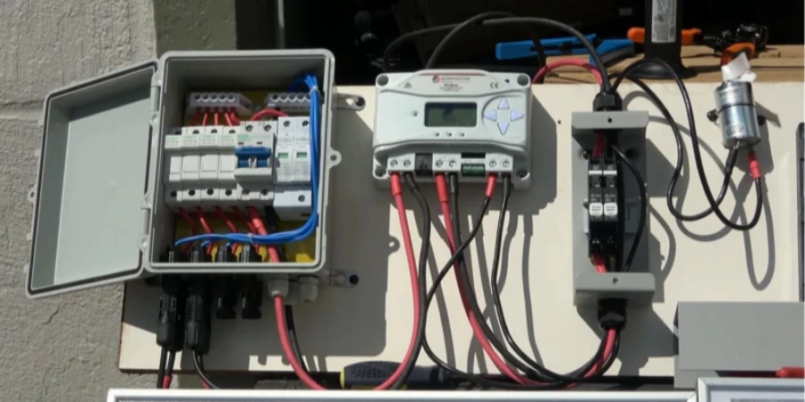 On the left side is a solar electrical setup mounted on a white board, featuring an open gray junction box that contains fuses, surge protection devices, and connected red and blue cables. The setup represents the protective and wiring components used in a solar power system.
