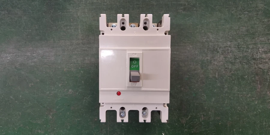 A white three-pole electrical circuit breaker placed on a green surface. The switch handle is in the down