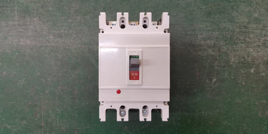 A white three-pole electrical circuit breaker placed on a green surface. The switch handle is in the middle tripped position, with a green