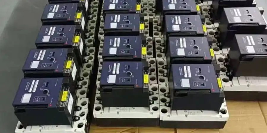 Multiple black molded case circuit breakers (MCCBs) arranged in rows on mounting bases. Each MCCB has a motorized operating mechanism module mounted on top with control buttons, indicator lights, and adjustment knobs for remote operation.