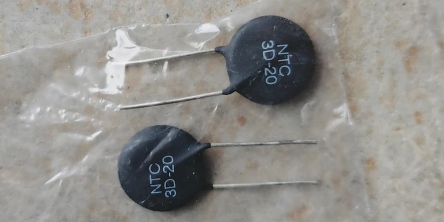 Two black disc-shaped NTC thermistors with metal leads, labeled 'NTC 20 3D' and 'NTC 30 3D', lying on a clear plastic bag over a light-colored surface.