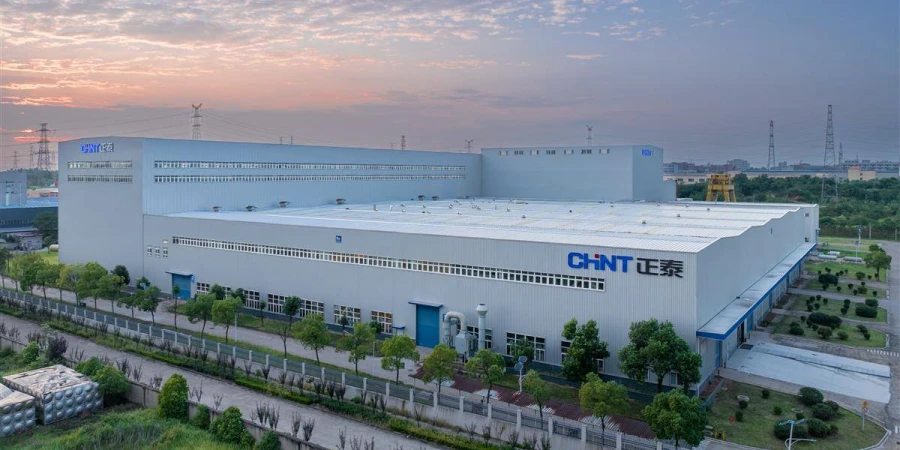 Aerial view of a large modern industrial building with CHINT logo and Chinese characters on the facade, surrounded by green trees and pathways, under a sunset sky in Liushi