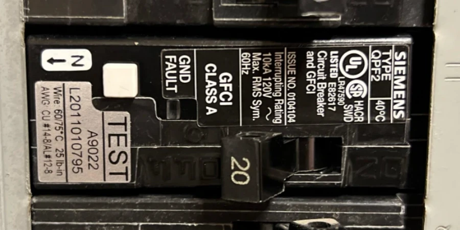A close-up of a black Siemens Type QPF2 GFCI circuit breaker in an electrical panel. The breaker is rated 20 amps, with a white test button labeled 'TEST' on the left and a black toggle switch in the off position. Labels show it is UL listed, Class A GFCI, for 120V, with interrupting rating 10kA.